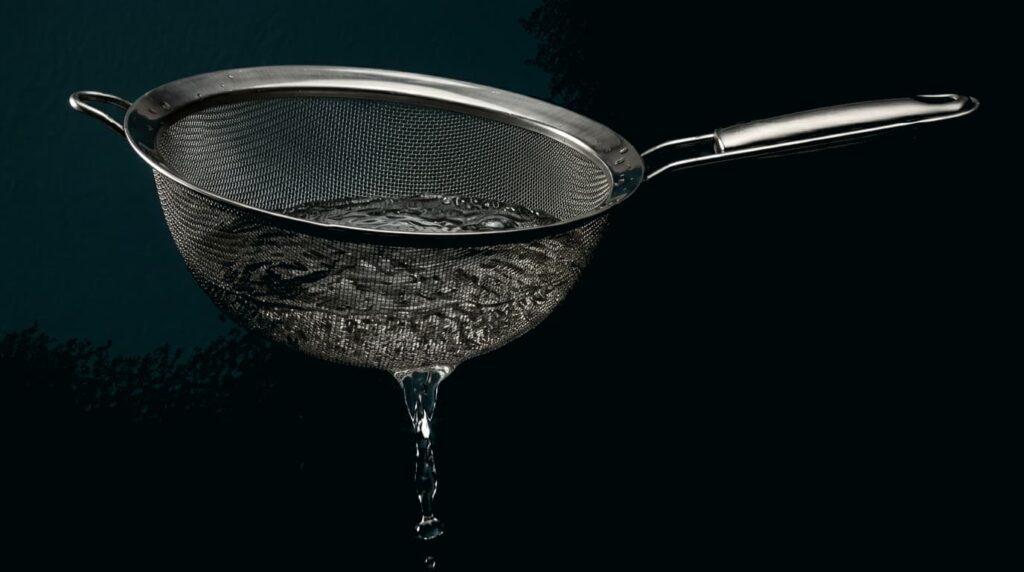 colador con agua escapándose, metáfora visual de controlar gastos variables mes a mes